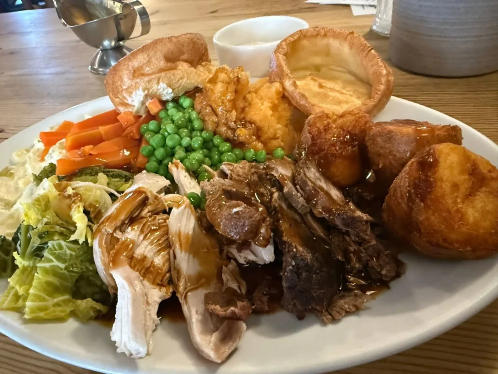 a roast dinner served with chicken, beef, carrots, peas, Yorkshire puddings, and gravy